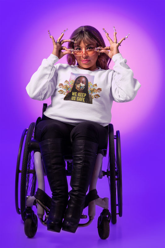 Seated in a wheelchair against a purple backdrop, a person radiates the vibrant spirit of Jennifer White-Johnson's Disability Culture Lab. They wear glasses, black pants, and stylish long nails while confidently adorned in the "We Keep Us Safe" sweatshirt from Disability Culture Lab. Their playful expression is elegantly framed by expertly manicured fingers.