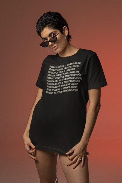 A person wearing sunglasses and large hoop earrings stands confidently against a red gradient background, showcasing the "Disability Justice Is Tee" by Disability Culture Lab.